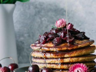 a stack of pancakes on a blue plate with summer cherries and flowers and the words "black cherry hoecakes" in black writing