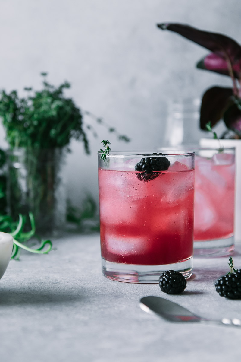 a blackberry infused sparkling water in a cocktail glass on a grey table