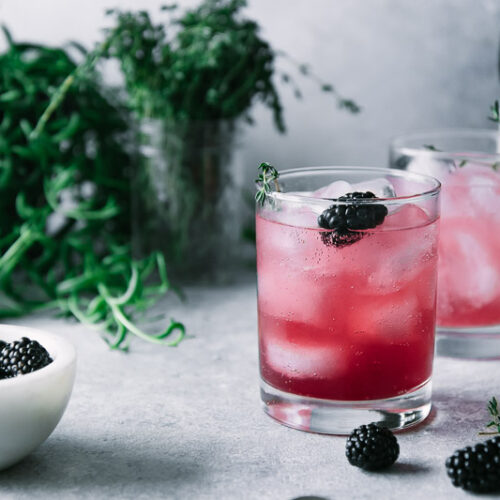 a glass of blackberry-infused sparkling water with fresh thyme in the background