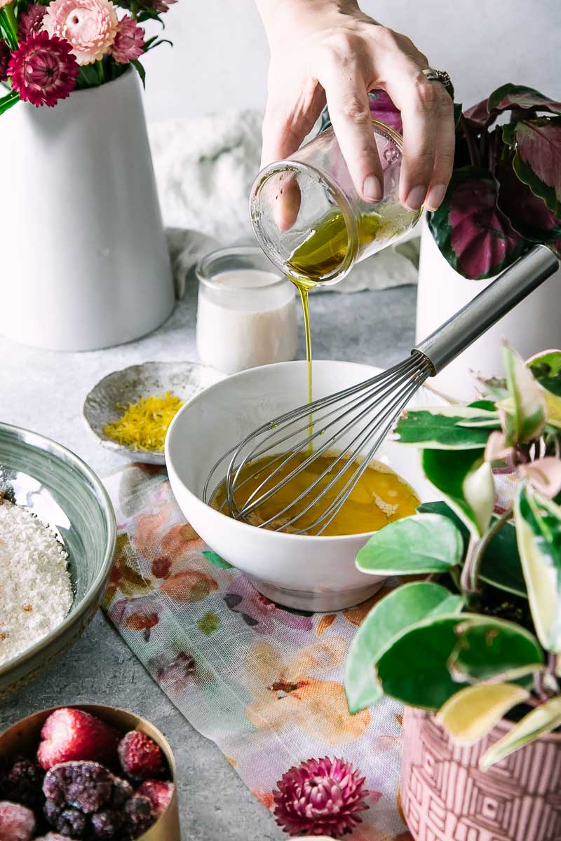 a hand pouring oil into a bowl with cracked eggs to make cornbread muffins