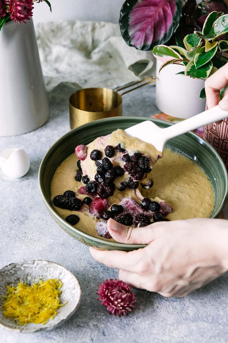 a hand mixing berries into muffin batter on a white table with flowers