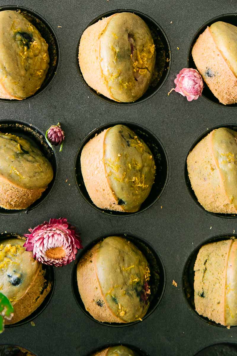 baked berry and lemon muffins in a muffin tin with flowers