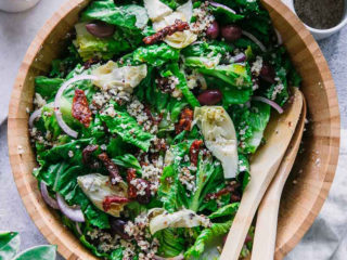 a salad mixing bowl with a greek salad with quinoa inside