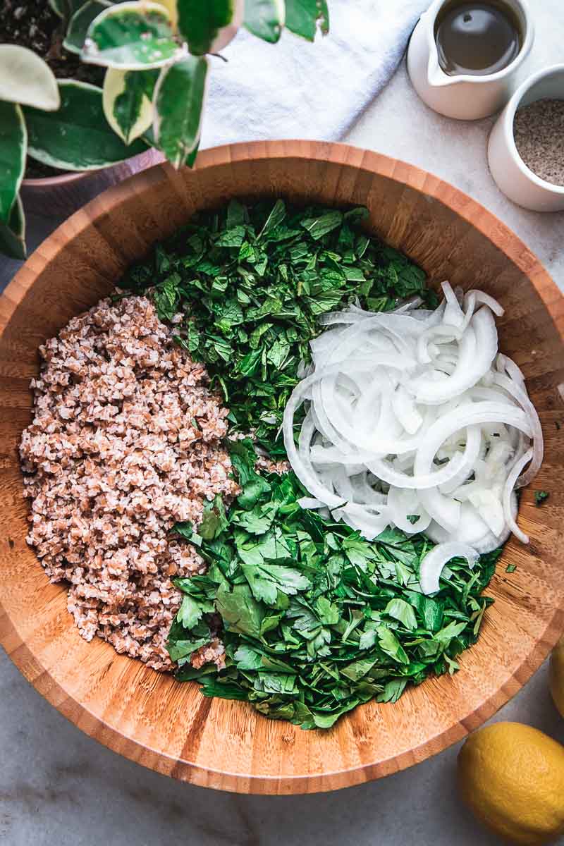 a wooden mixing bowl filled with bulgur, chopped onion, and fresh parsley and mint for a tabbouleh salad