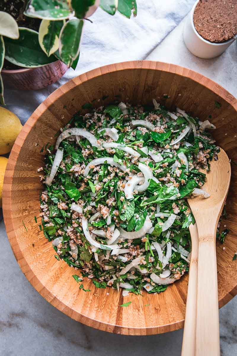 a wooden salad bowl with mixed bulgur tabbouleh and a wooden spoon on a white table with lemons