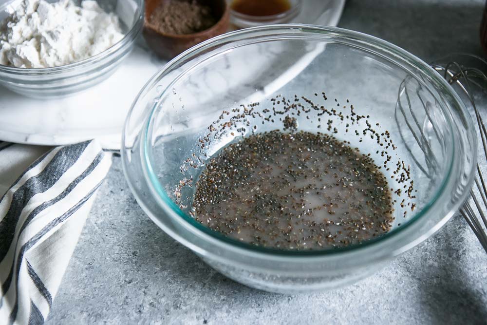 a glass bowl with a flax egg made of flax seed, water, and chia seeds on a blue table