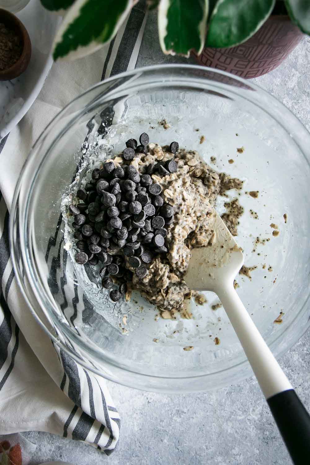 a glass mixing bowl with vegan oatmeal cookie batter and chocolate chips indie with a white spoon