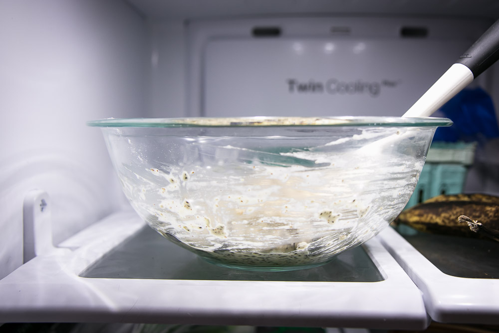 a glass mixing bowl with vegan oatmeal chocolate chip cookie batter on a refrigerator shelf