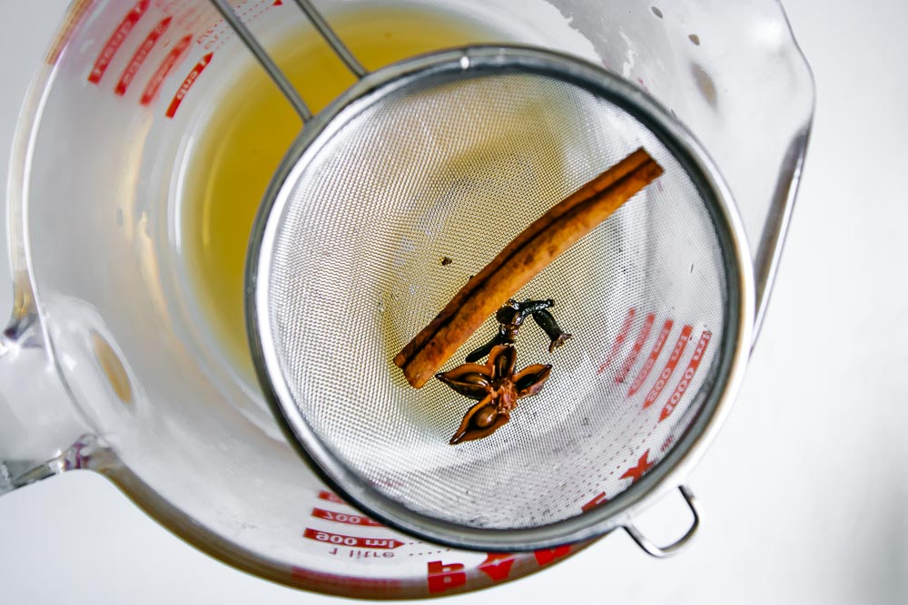 strained whole spices like cinnamon stick, cloves, and anise over a bowl of apple cider vinegar liquid