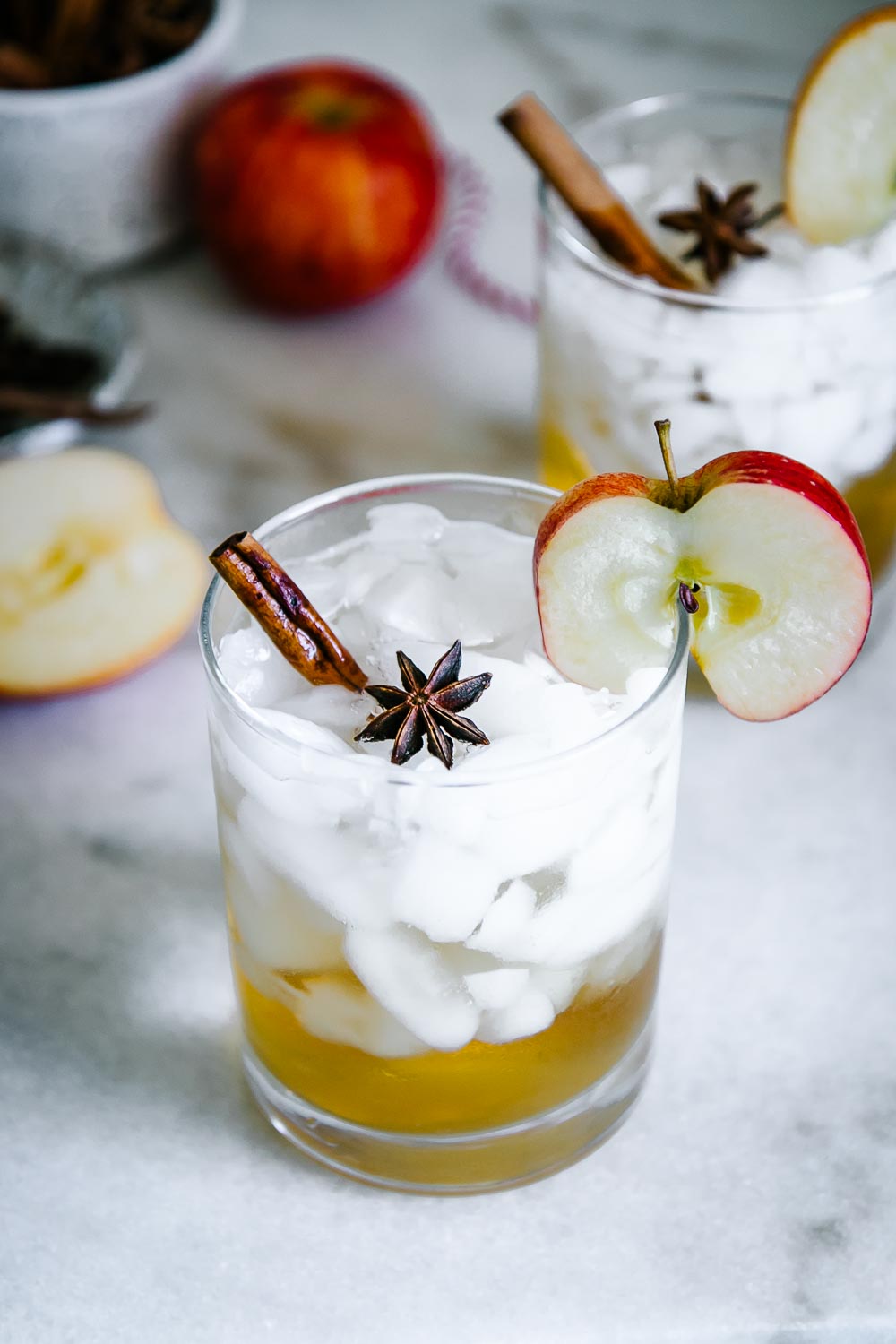 a mocktail glass with ice and apple cider sparkling water with an apple slice and a cinnamon stick