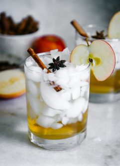 a glass with ice and apple cider vinegar and sparkline water with an apple slice garnish on a white table
