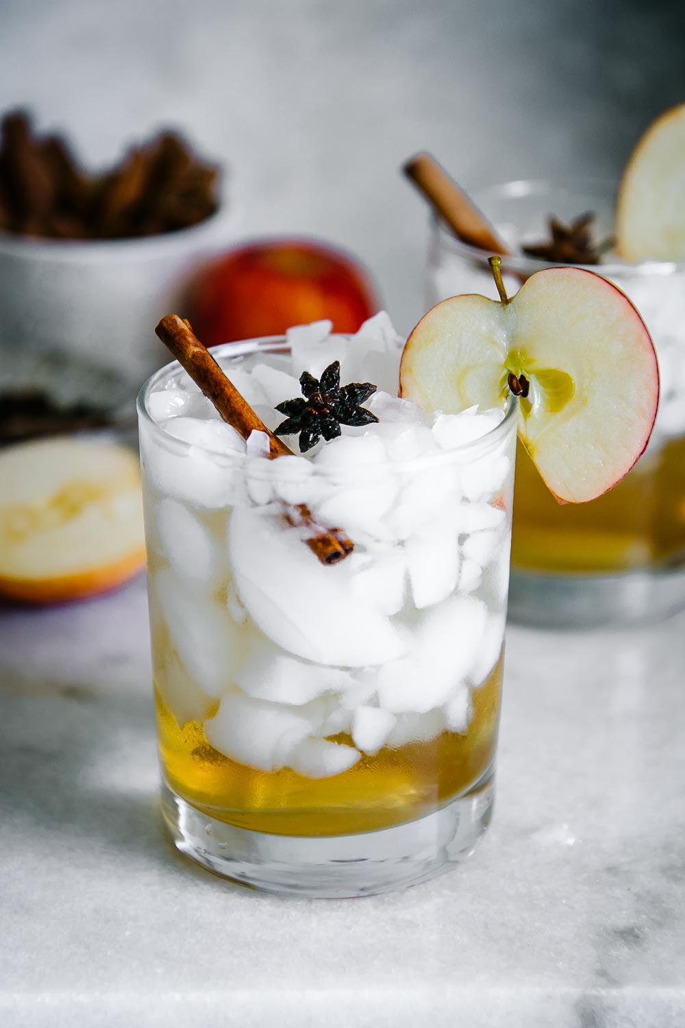 a glass with ice and apple cider vinegar and sparkline water with an apple slice garnish on a white table