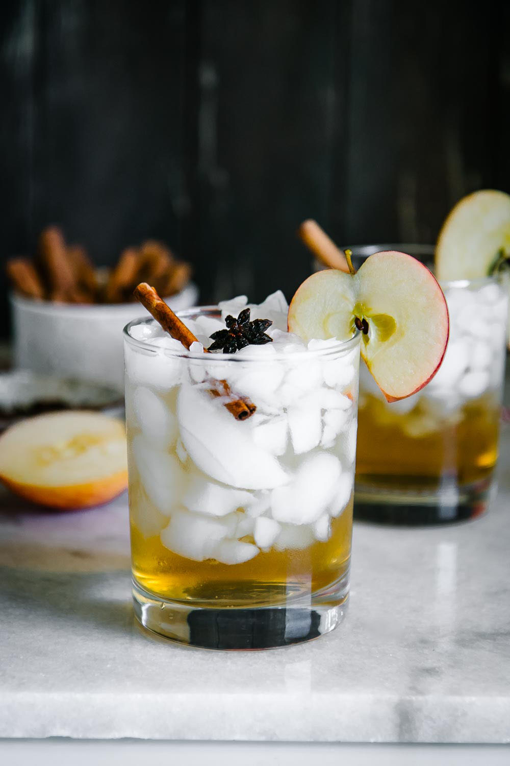 a cocktail glass with ice and apple cider spritzer on a white marble table with a black background