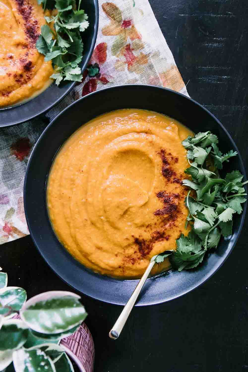 a bowl of sweet potato and carrot soup with cilantro as garnish on a wood table with a gold spoon