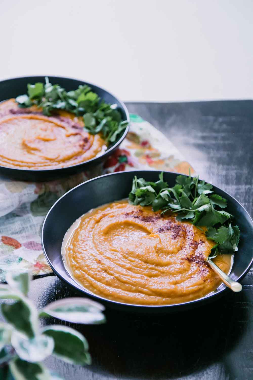 sweet potato carrot soup in two black bowls on a dark wood table with a floral napkin