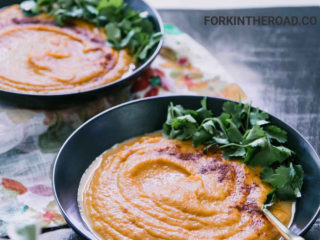 two black bowls with orange sweet potato carrot soup on a wood table with the words "Sweet Potato Carrot Soup" in orange and black writing