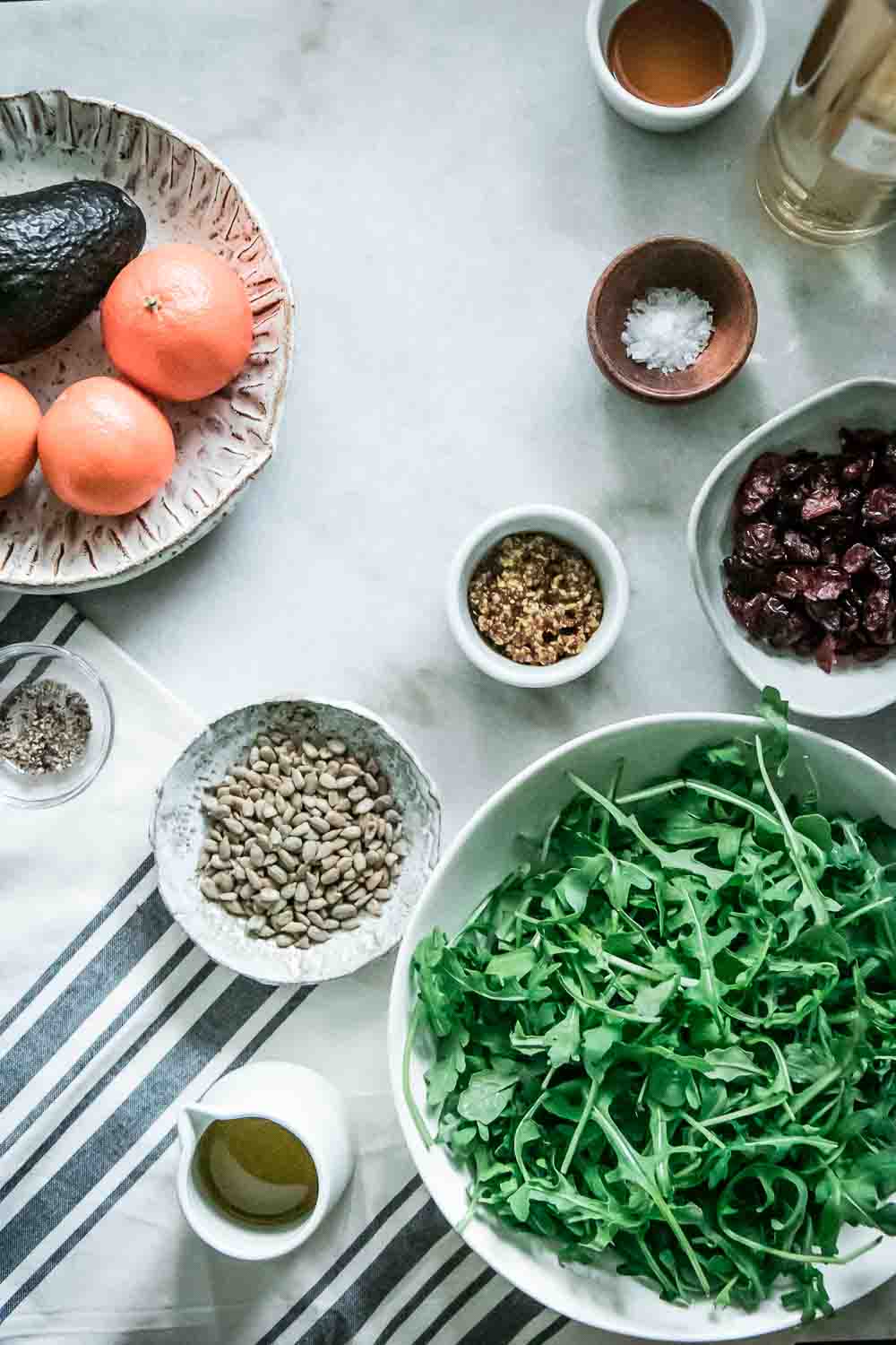 arugula, sunflower seeds, cranberries, oranges, and avocado on a marble table