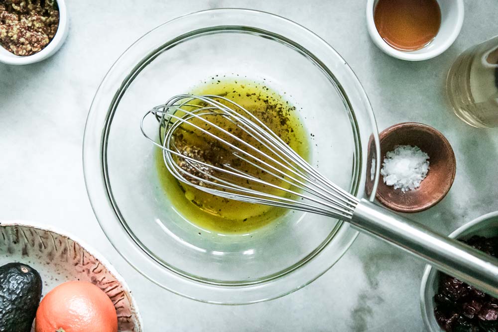 a bowl of white wine vinaigrette salad dressing with a silver whisk on a white table
