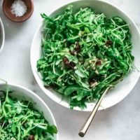 arugula salad with cranberries and sunflower seeds in a white bowl on a marble table