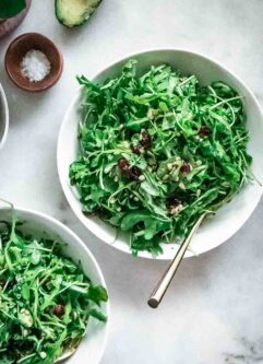 arugula salad with cranberries and sunflower seeds in a white bowl on a marble table