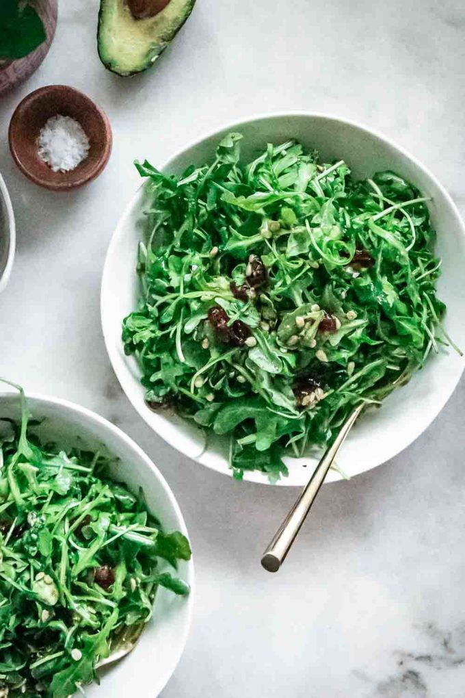 arugula salad with cranberries and sunflower seeds in a white bowl on a marble table