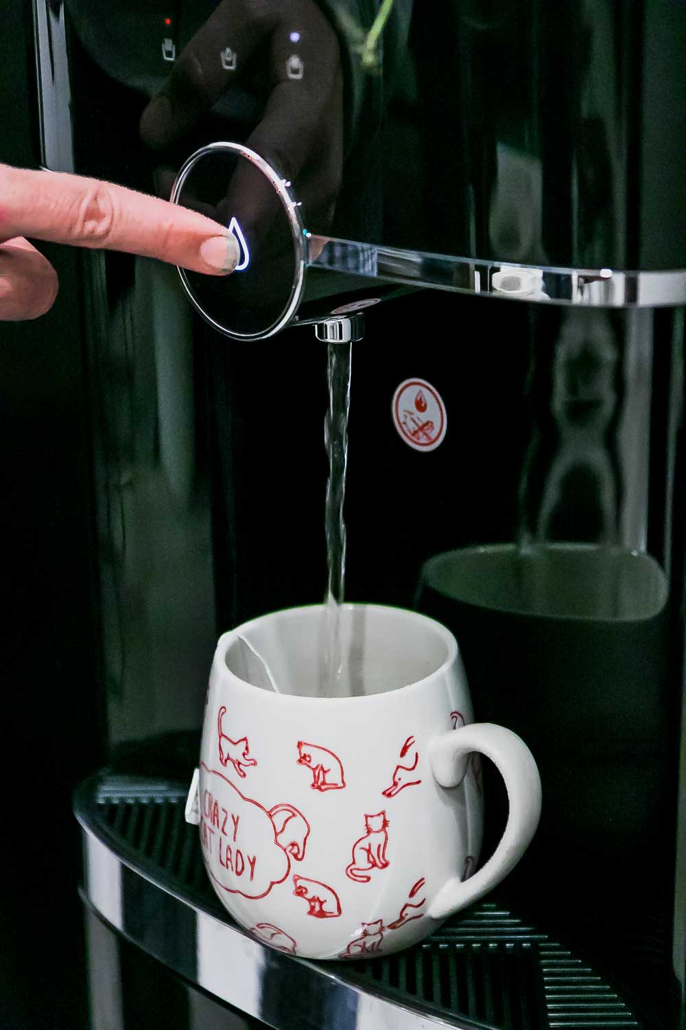 a finger dispensing water from a primo water dispenser into a coffee cup