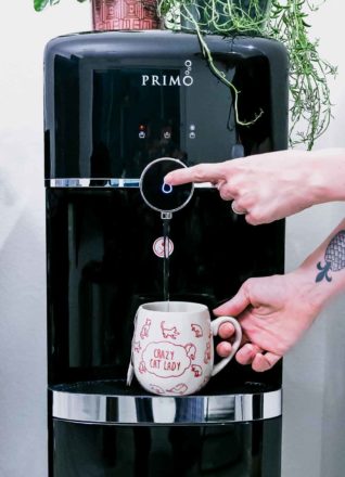 two hands dispensing water into a coffee cup from a Primo water dispenser
