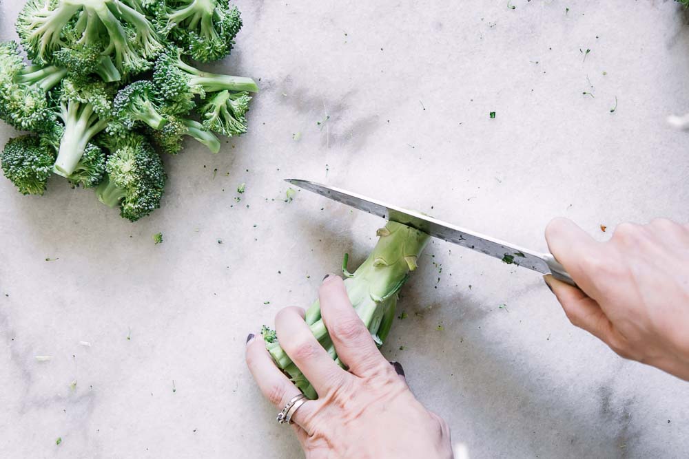 a hand cutting the florets off broccoli stalks