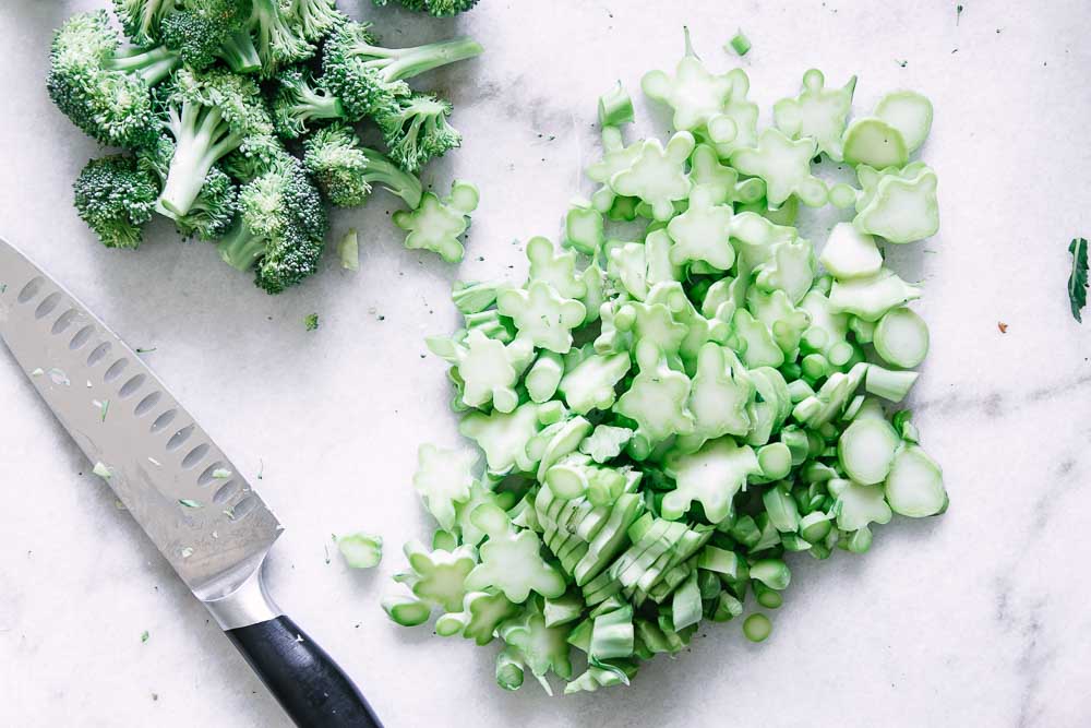 cut broccoli stems from stalks on a white marble table with a knife