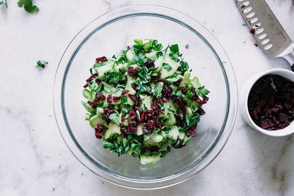 a glass mixing bowl with broccoli stems, cranberries, and chopped cilantro