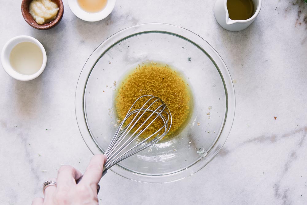 a hand whisking together salad dressing on a white table