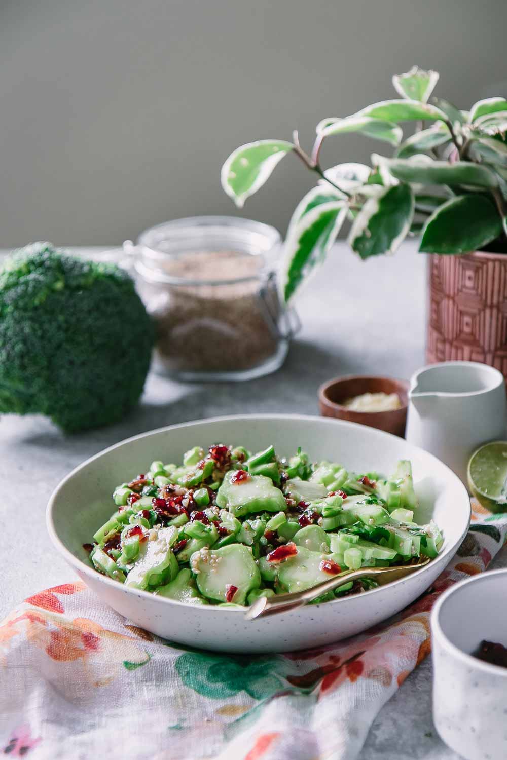 a white bowl with broccoli stems and cranberries in a white bowl on a blue table and a plant in the background