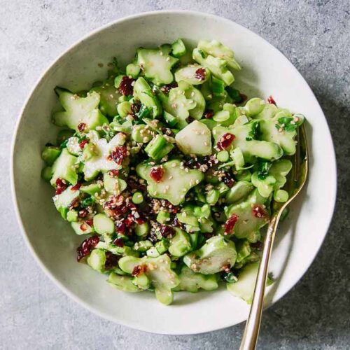 a white bowl with a green broccoli stem and cranberry salad with a gold fork on a blue table