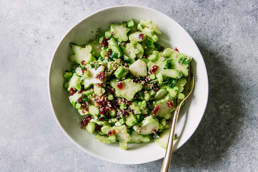 a white bowl with a green broccoli stem and cranberry salad with a gold fork on a blue table