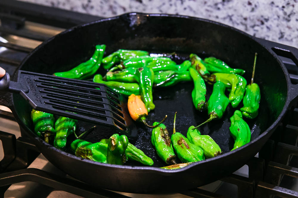 shishito peppers in a cast iron skillet with a black spatula