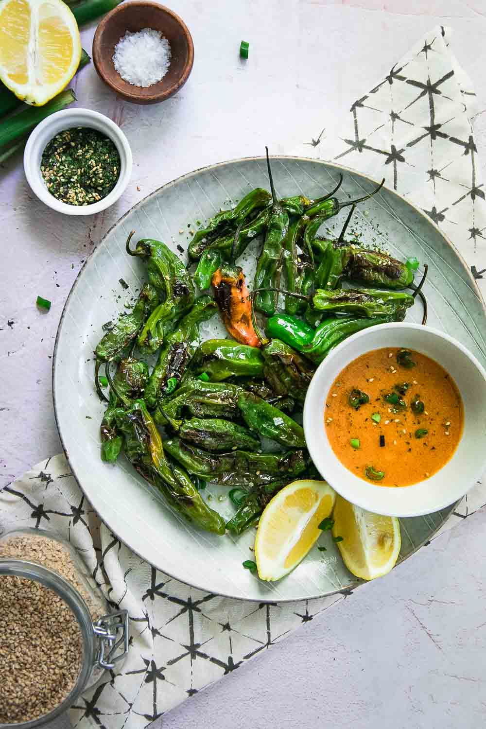 a blue plate with green shishito peppers, an orange dipping sauce, and a lemon wedge