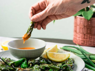 a hand dipping a shishito pepper into an orange sauce with the words 