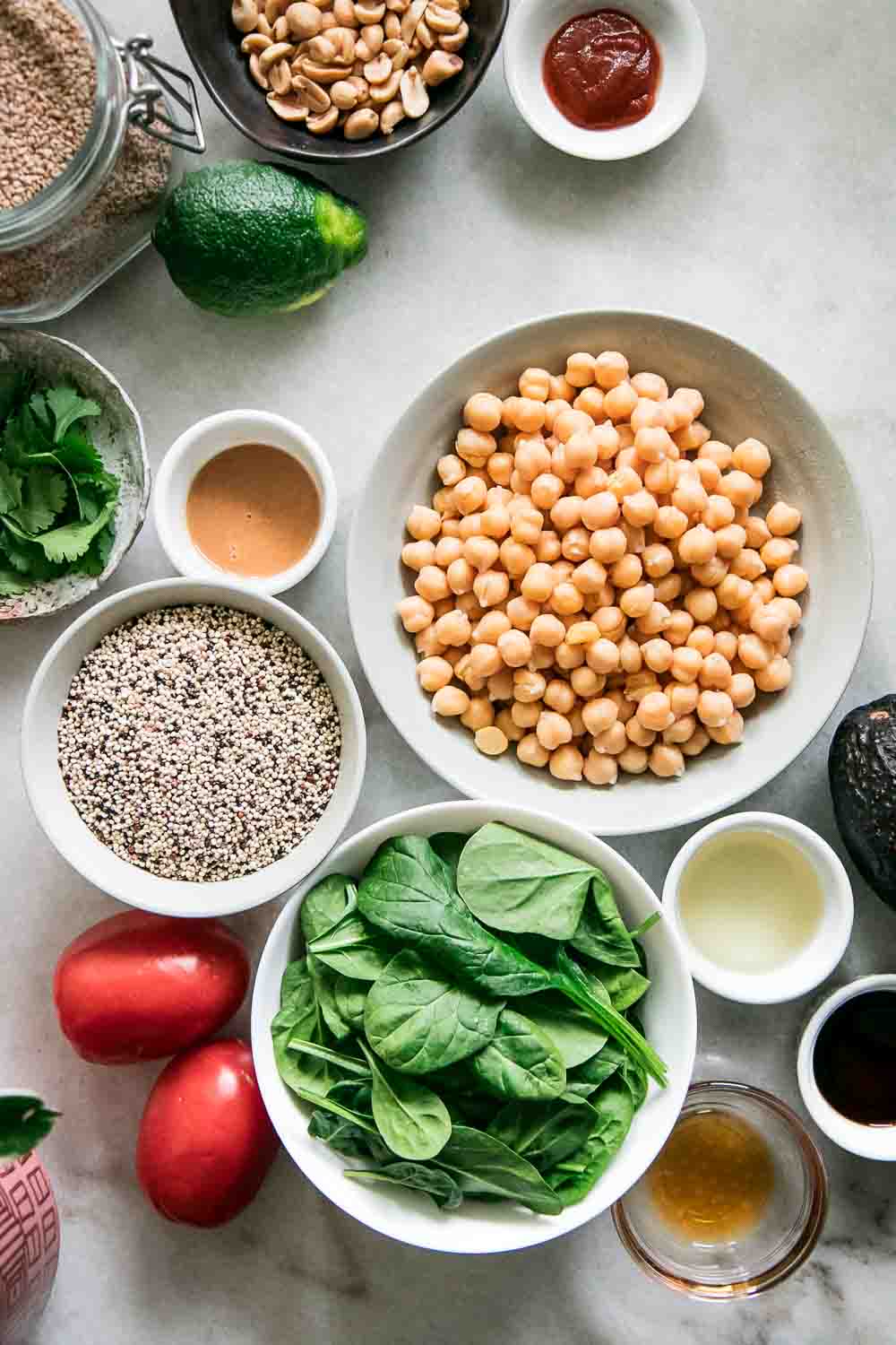 bowls of chickpeas, spinach, quinoa, sesame seeds, and tomatoes on a white table