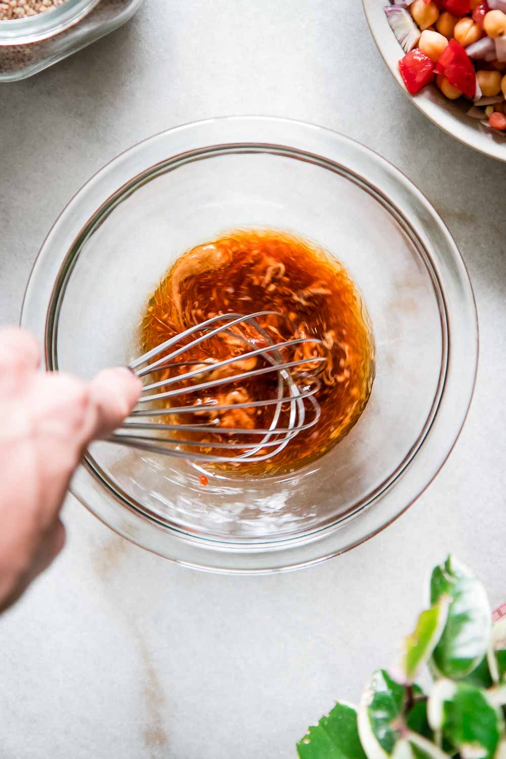 a hand whisking sauce in a glass mixing bowl on a white table