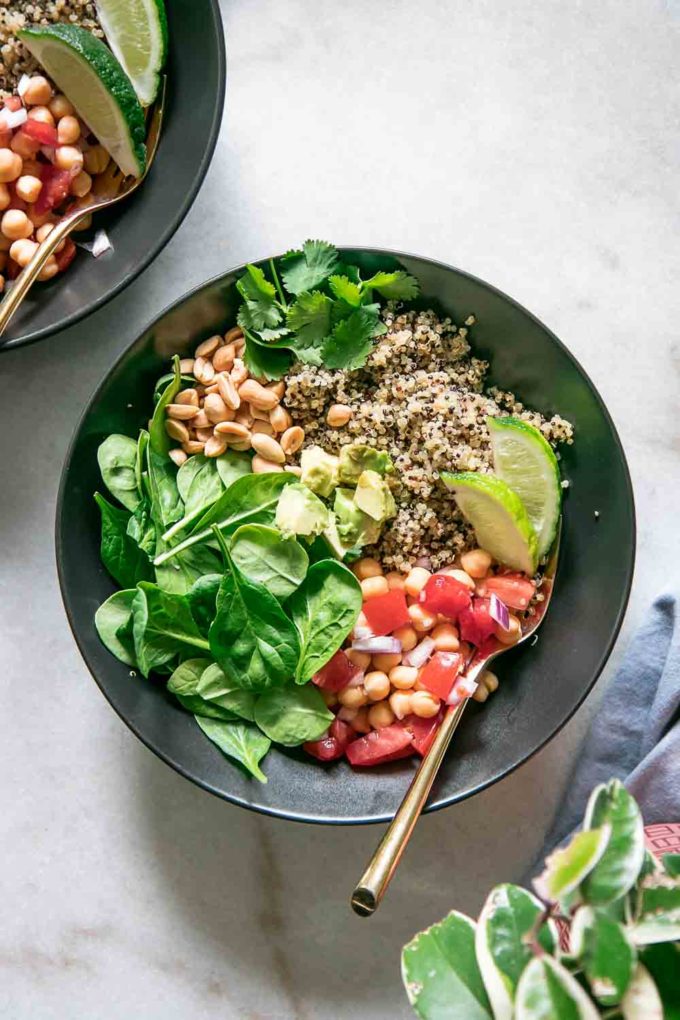 a black bowl filled with quinoa, spinach, chickpeas, and limes with a gold spoon on a white table