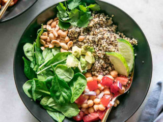 a black bowl with grains and vegetables on a white table with the words "Spicy Peanut Quinoa Bowl"