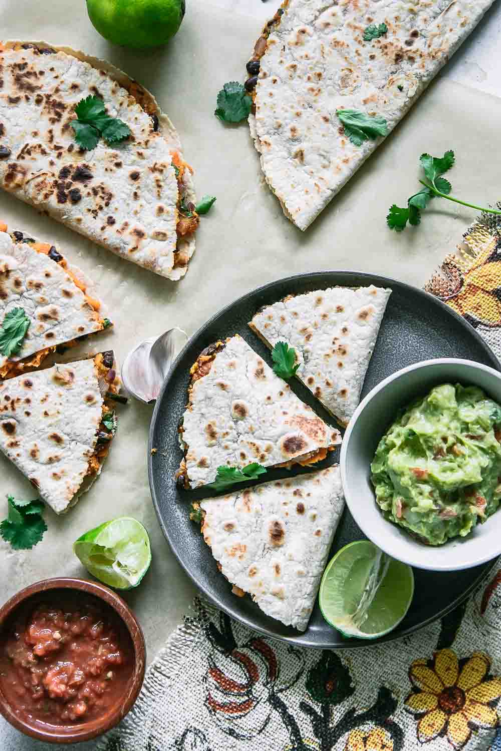 three quesadillas made of sweet potatoes on a plate and a table with a lime and guacamole