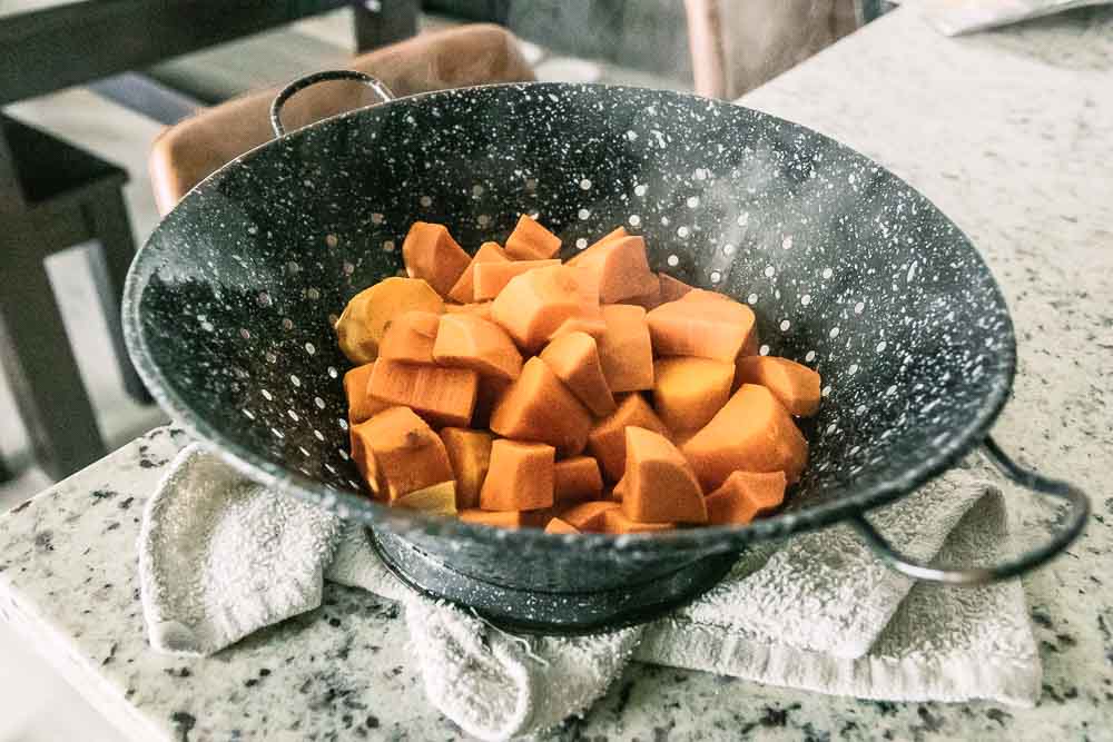 a blue colander with drained diced sweet potato on a kitchen counter
