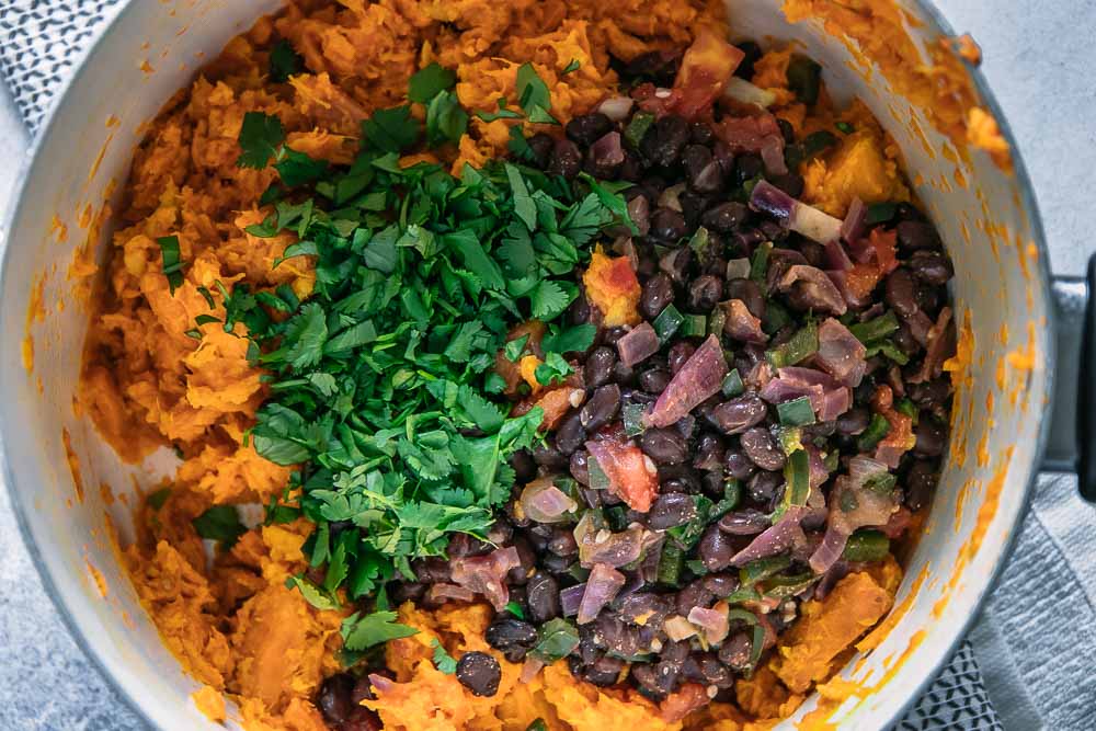 a close up photo of the inside of a white pot with mashed sweet potatoes, black beans, and chopped cilantro