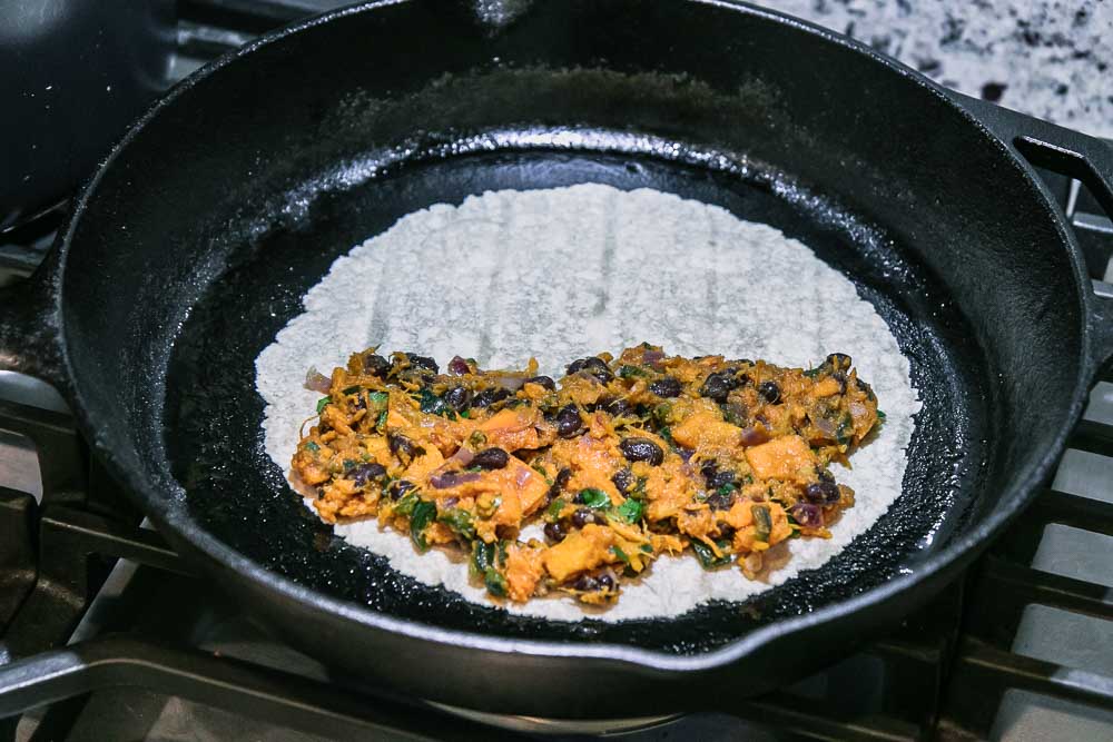 a cast iron skillet on a stovetop with an open tortillas and sweet potatoes and black beans on top