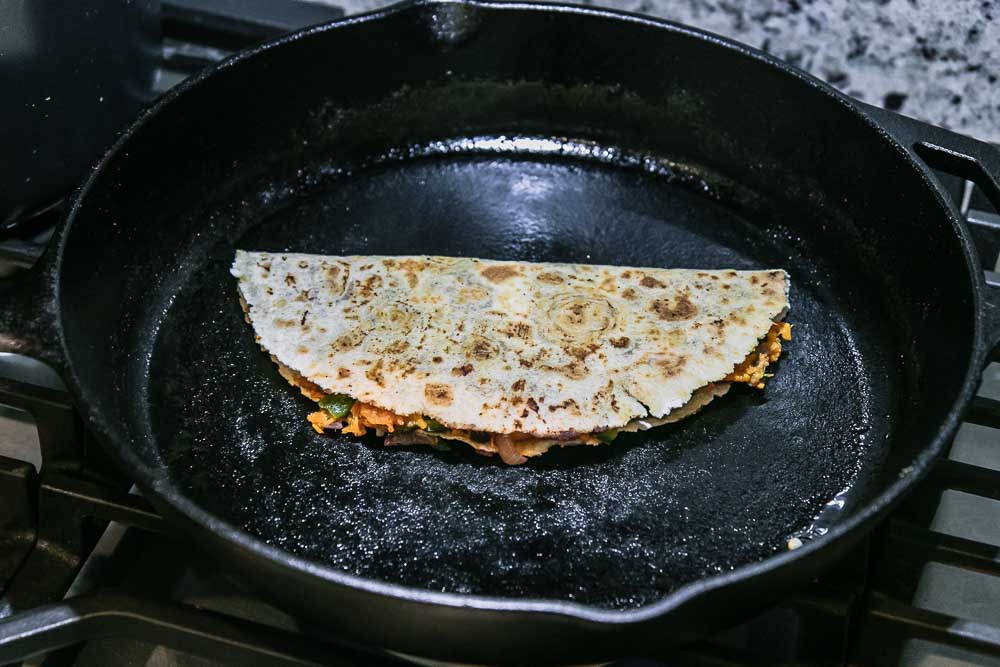 a folded tortilla filled with sweet potato and black beans in a black cast iron skillet on a stovetop