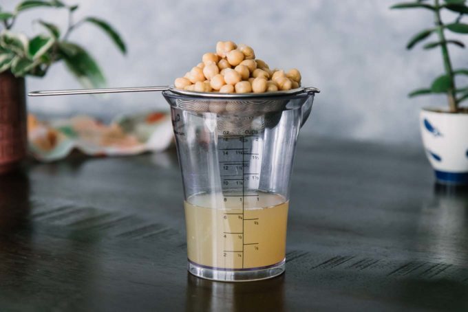 a cup of aquafaba, or chickpea water, drained into a glass jar with a strainer of chickpeas on top