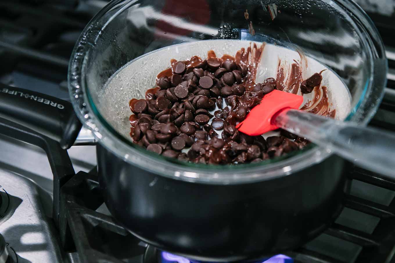 chocolate chips melting in a glass bowl in a hot water bath over a pot of warm water on the stove