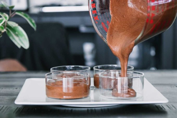 chocolate pouring into a glass bowls from a measuring cup on a wood table