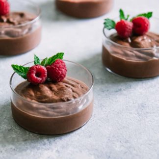 small round glass bowls of chocolate mousse with raspberries and mint on top of a blue table